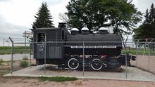 Black locomotive steam engine behind a chain link fence