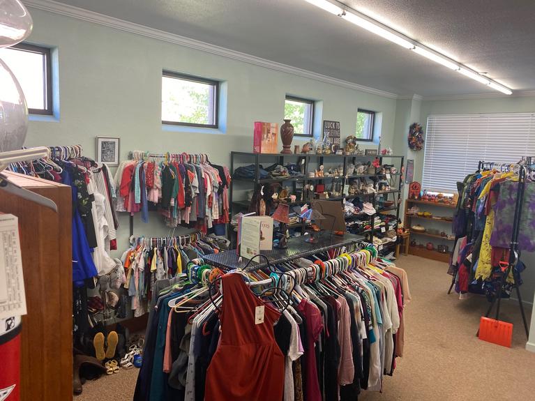 A small room with used clothing and housewares for sale hung on racks and on shelves